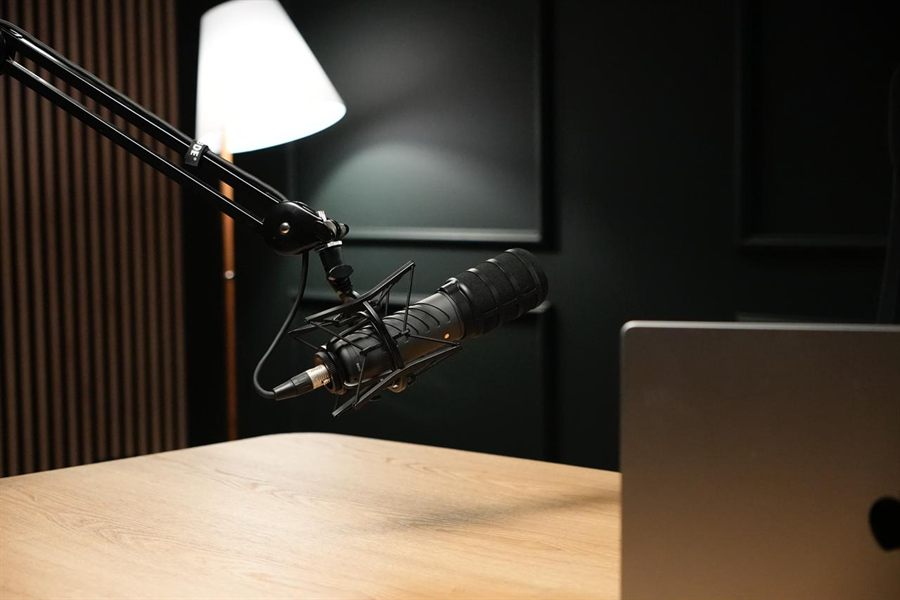 Boom-arm microphone over a light desk, dark green wall behind